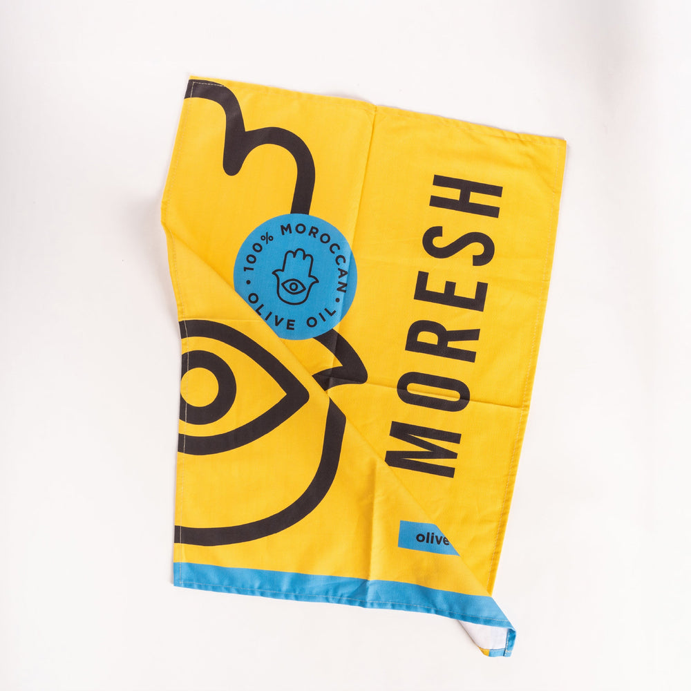 Moresh yellow tea towel laid flat against a white background, highlighting its clean edges, soft fabric texture, and minimalist logo design.